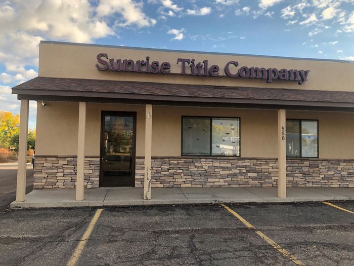 Storefront of Sunrise Title Company with beige walls and stone trim, viewed from the parking lot