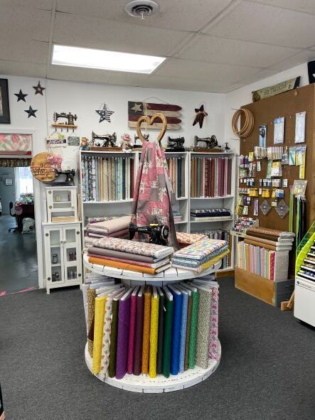 Craft store aisle with colorful fabric rolls, shelves of supplies, and a central display rack