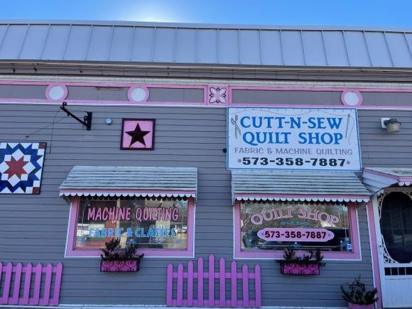 Quilt shop storefront with pink trim and signs reading “Cutt-N-Sew Quilt Shop” and “Machine Longarm Quilting”