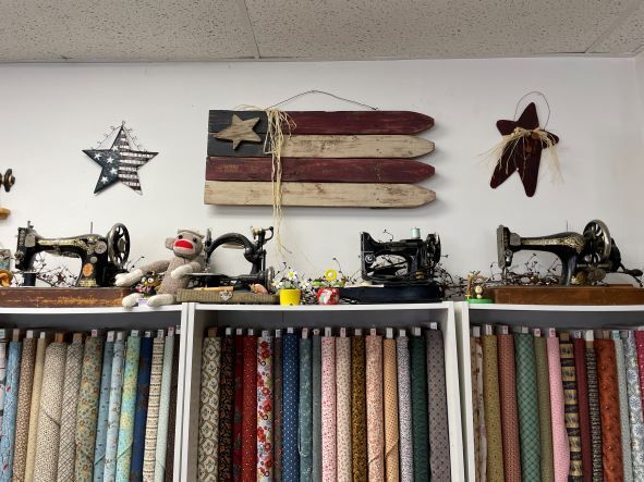 Quilt shop display with vintage sewing machines, fabric shelves, and rustic wall decor representing an American flag