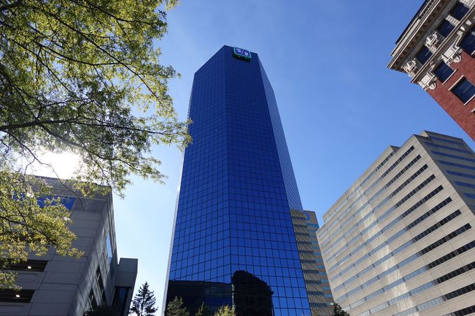 Blue glass skyscraper with other buildings and tree branches against a blue sky.
