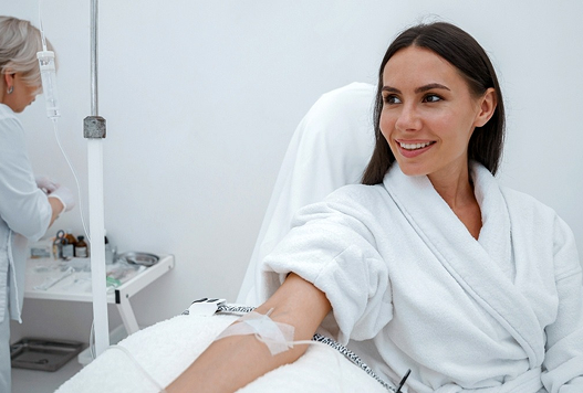 Woman in a spa robe receiving a treatment with an IV line in a bright clinic room