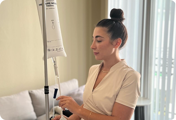 Woman preparing an IV drip in a well-lit room with a beige sofa.