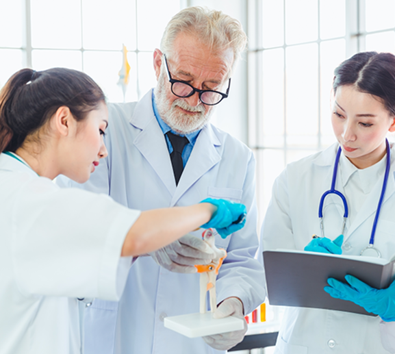 Three scientists in a lab examine a model, with one holding it, while another records notes.