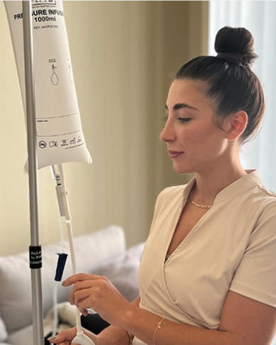 Woman seated beside an IV drip, adjusting the line in a clinical setting.