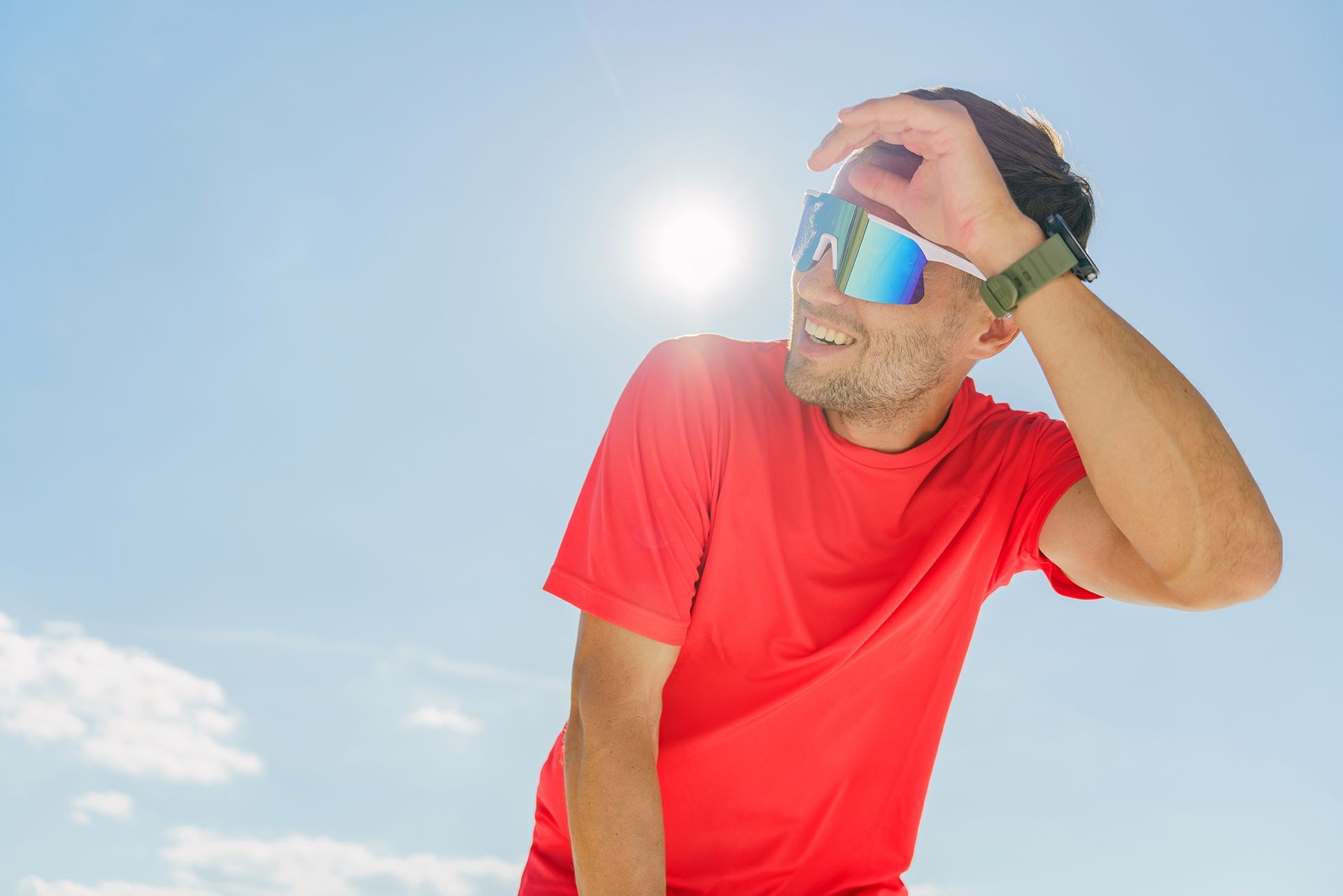 Man in red shirt shielding his eyes from bright sun under a clear blue sky