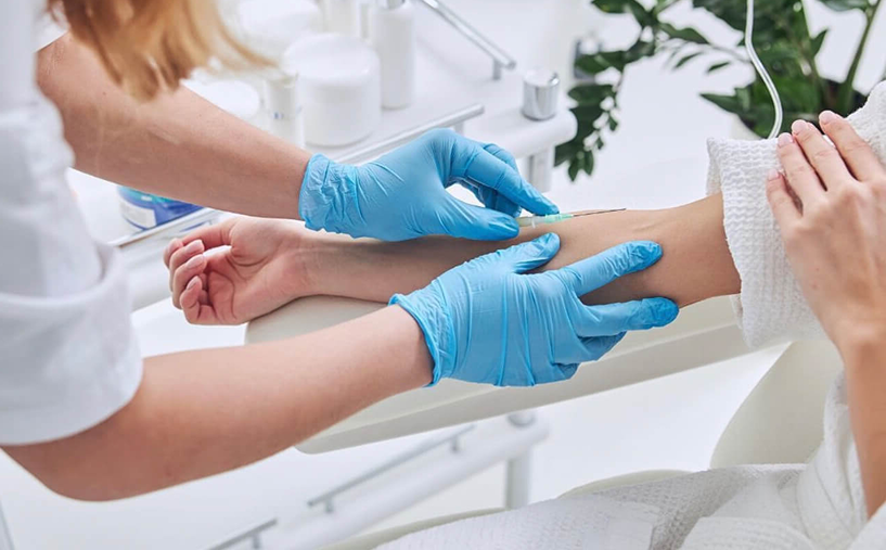 A person's arm being prepped for an IV by a healthcare worker wearing blue gloves.