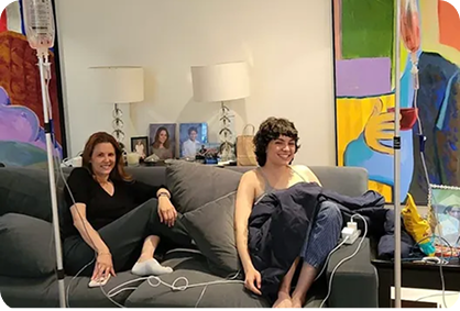 Two people sitting on a gray couch in a colorful living room, smiling and chatting with cables nearby