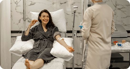 Woman receiving IV drip, smiling, in a spa-like setting. Nurse attends.