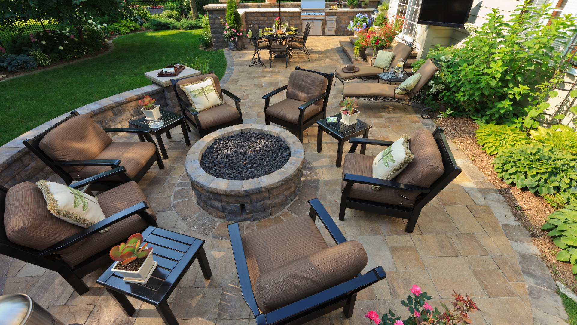 Outdoor patio with a circular fire pit, dark seating chairs, and potted plants on stone pavers