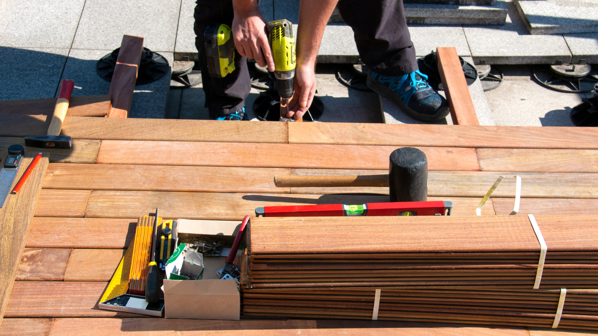 Workers installing wooden deck boards with tools on a rooftop construction site.