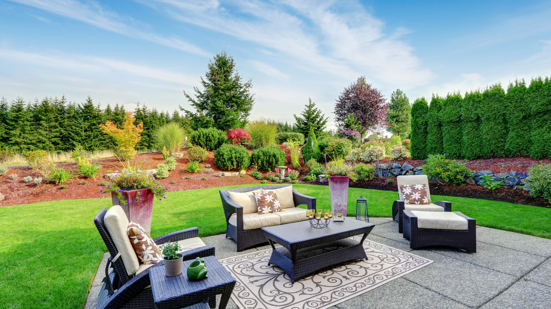 Backyard patio with wicker lounge chairs, black coffee table, and colorful garden landscaping