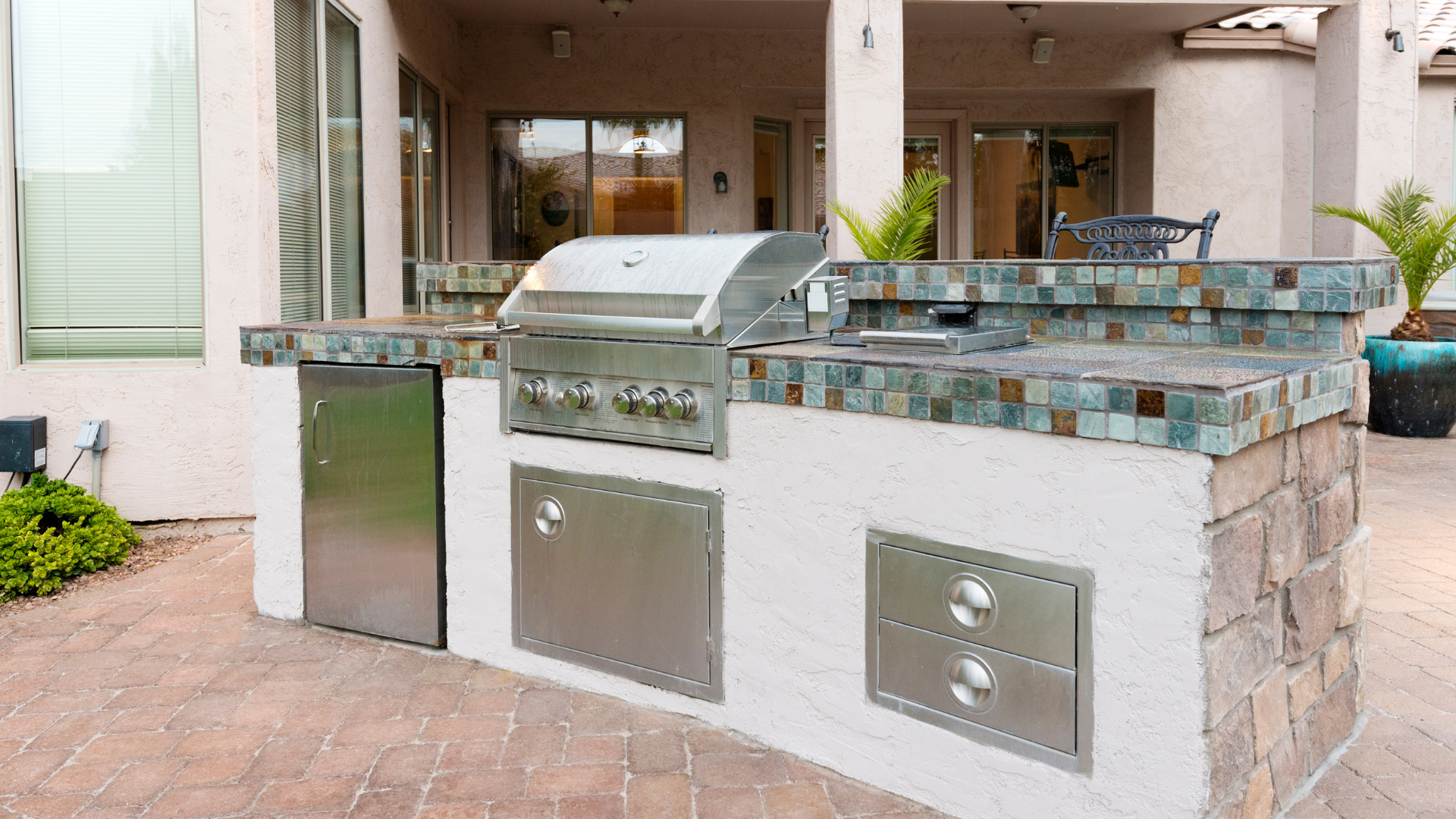 Outdoor built-in stainless steel grill and cabinets on a tiled patio under a covered patio area