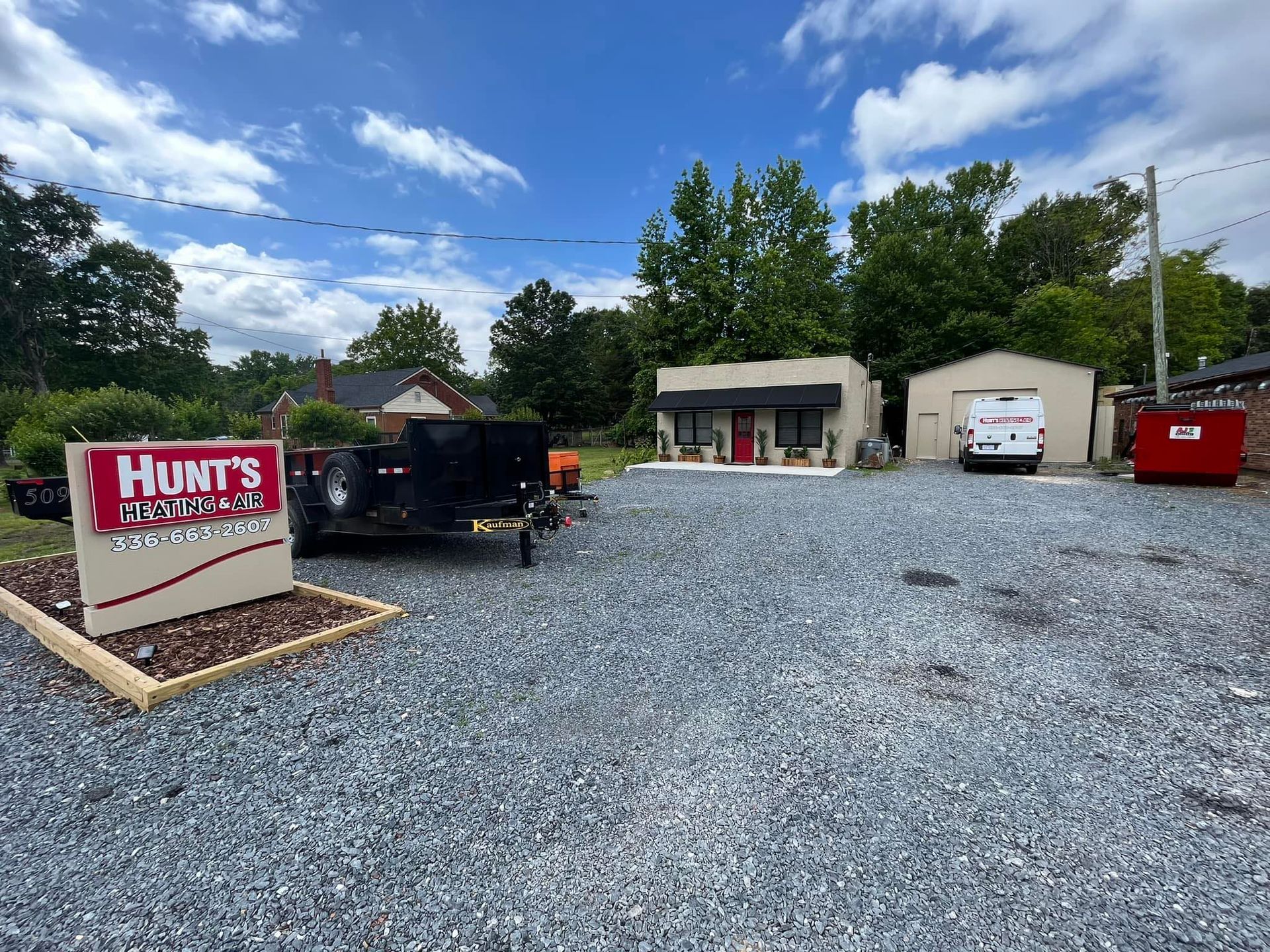 A sign for hunt 's trailers is in a gravel lot in front of a building.