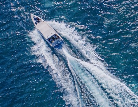 A long, white powerboat cuts through deep blue water, leaving a large, foamy white wake behind it.