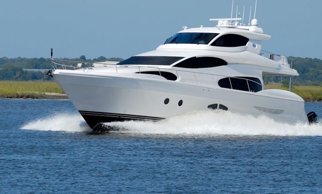A sleek, white motor yacht cruising across blue water on a sunny day with green marshland in the background.