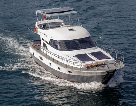 A white powerboat with solar panels on its roof and deck moves across blue water, leaving a wake behind it.