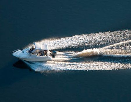A white motorboat with a canopy travels across calm, dark blue water, leaving a wide wake behind it.