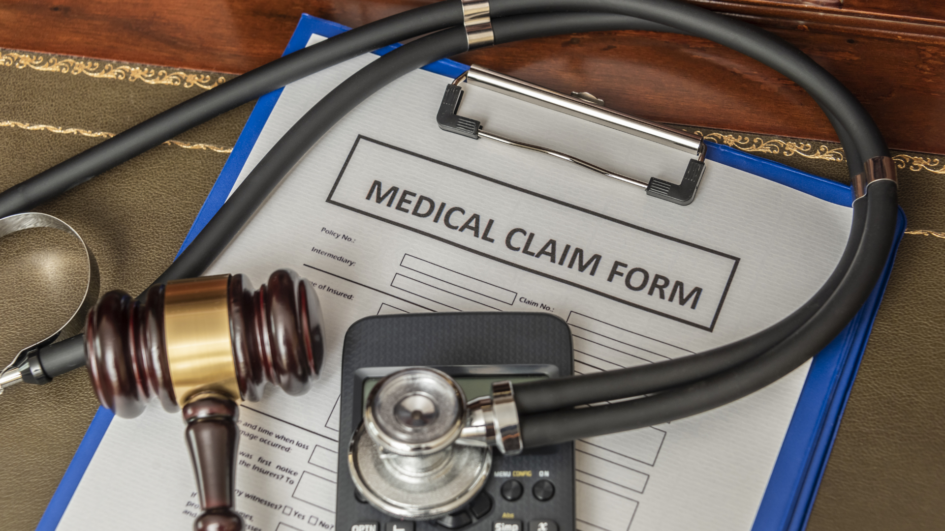 Medical claim form with stethoscope, gavel, and calculator on a desk.