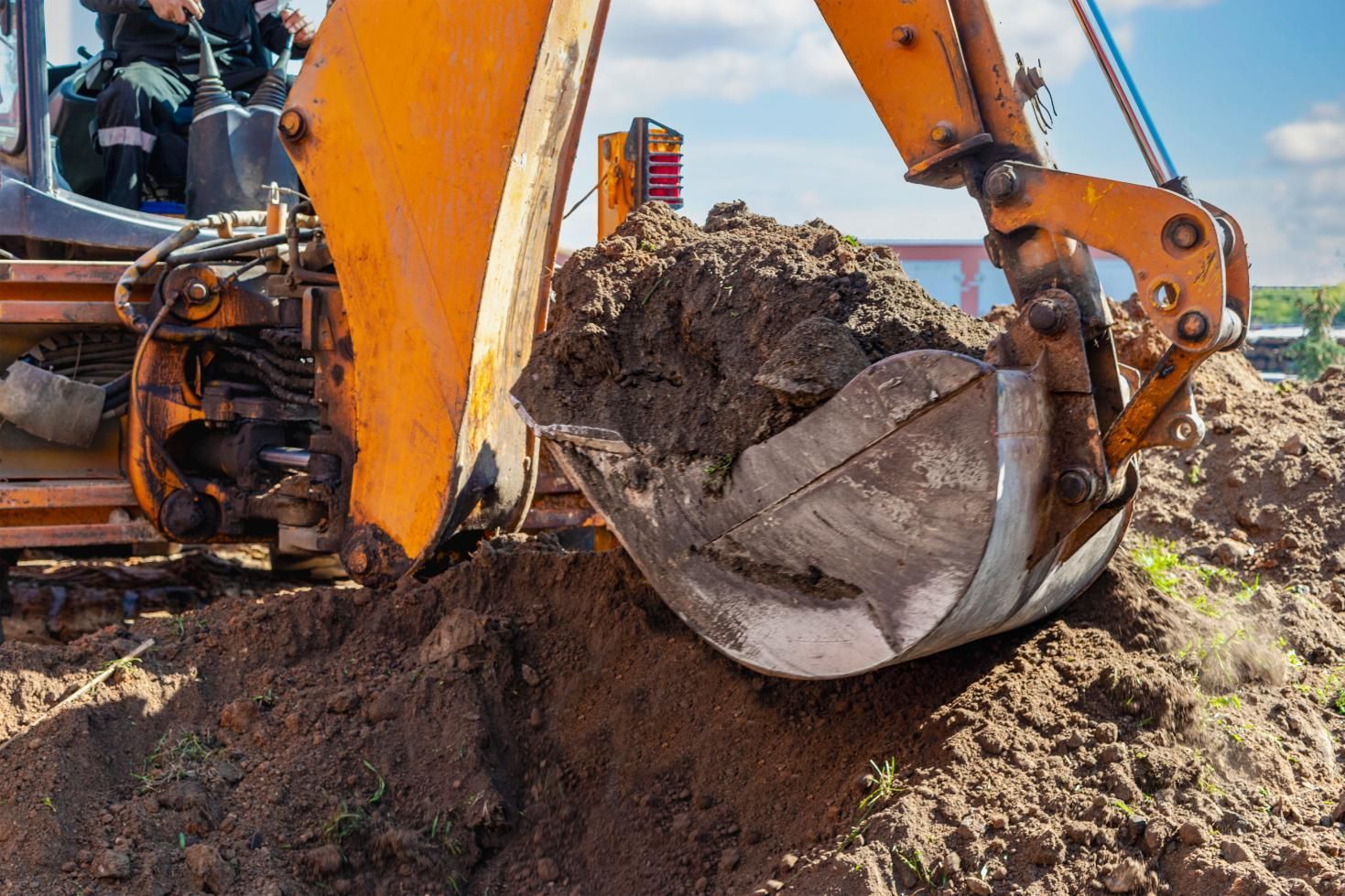 Excavator bucket lifting a load of dirt at a construction site under a blue sky