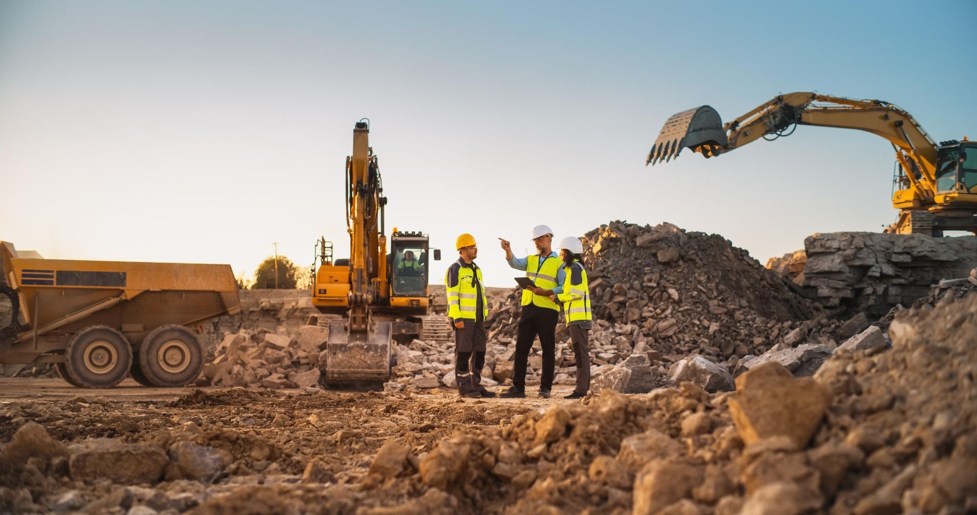 Construction workers and heavy machinery at a dirt excavation site at sunset