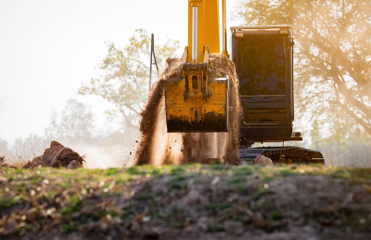 Yellow excavator digging soil on a construction site with dust in the air