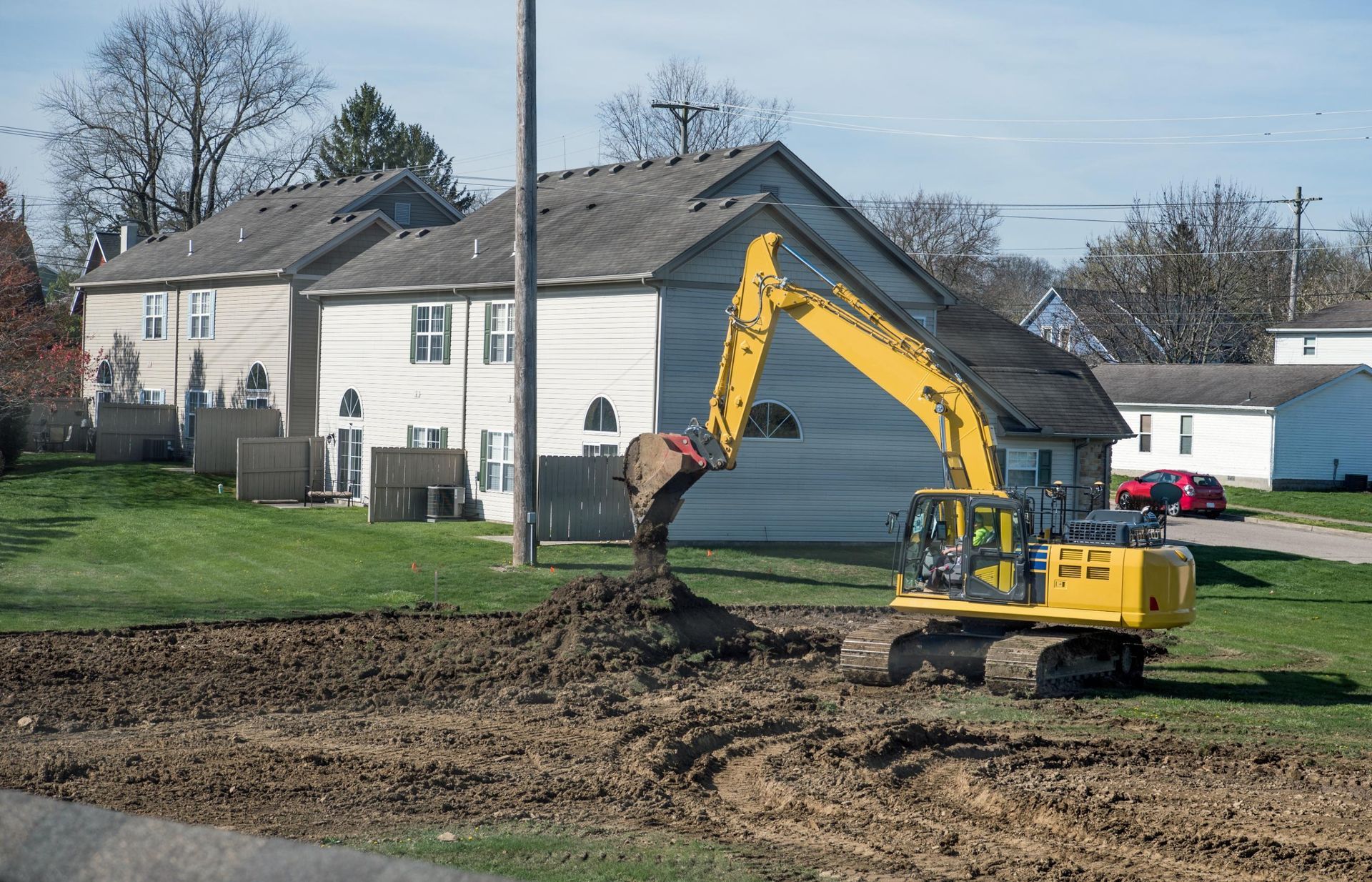 Yellow excavator digging dirt beside a white house on a residential lawn