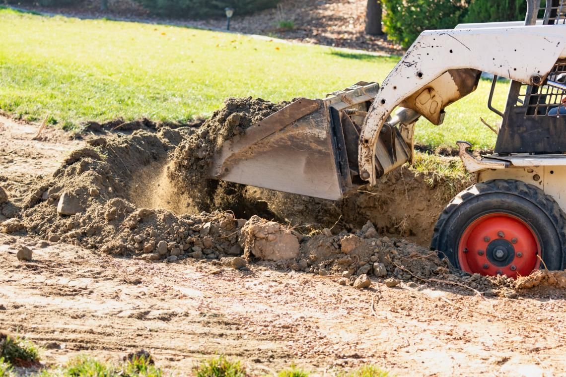 Backhoe loader digging dirt beside a muddy path, with a raised bucket and red wheel visible