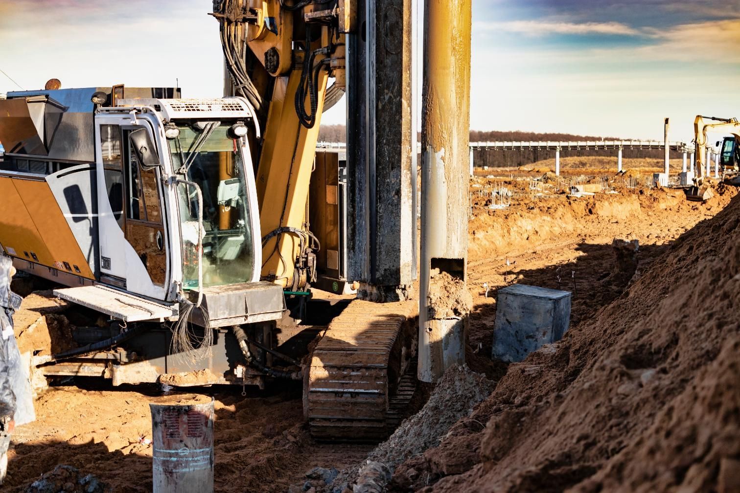 Excavator digging trench at a construction site beside a dump truck and dirt piles