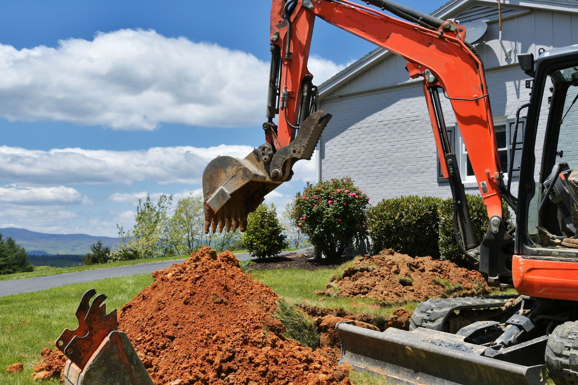 Excavator dumping soil into a pile beside a white building under a blue sky