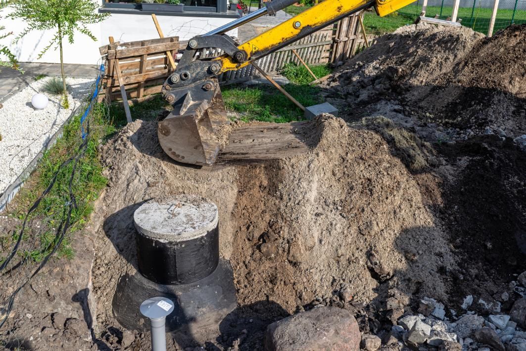 Excavator digging around a large concrete pipe in a muddy construction trench