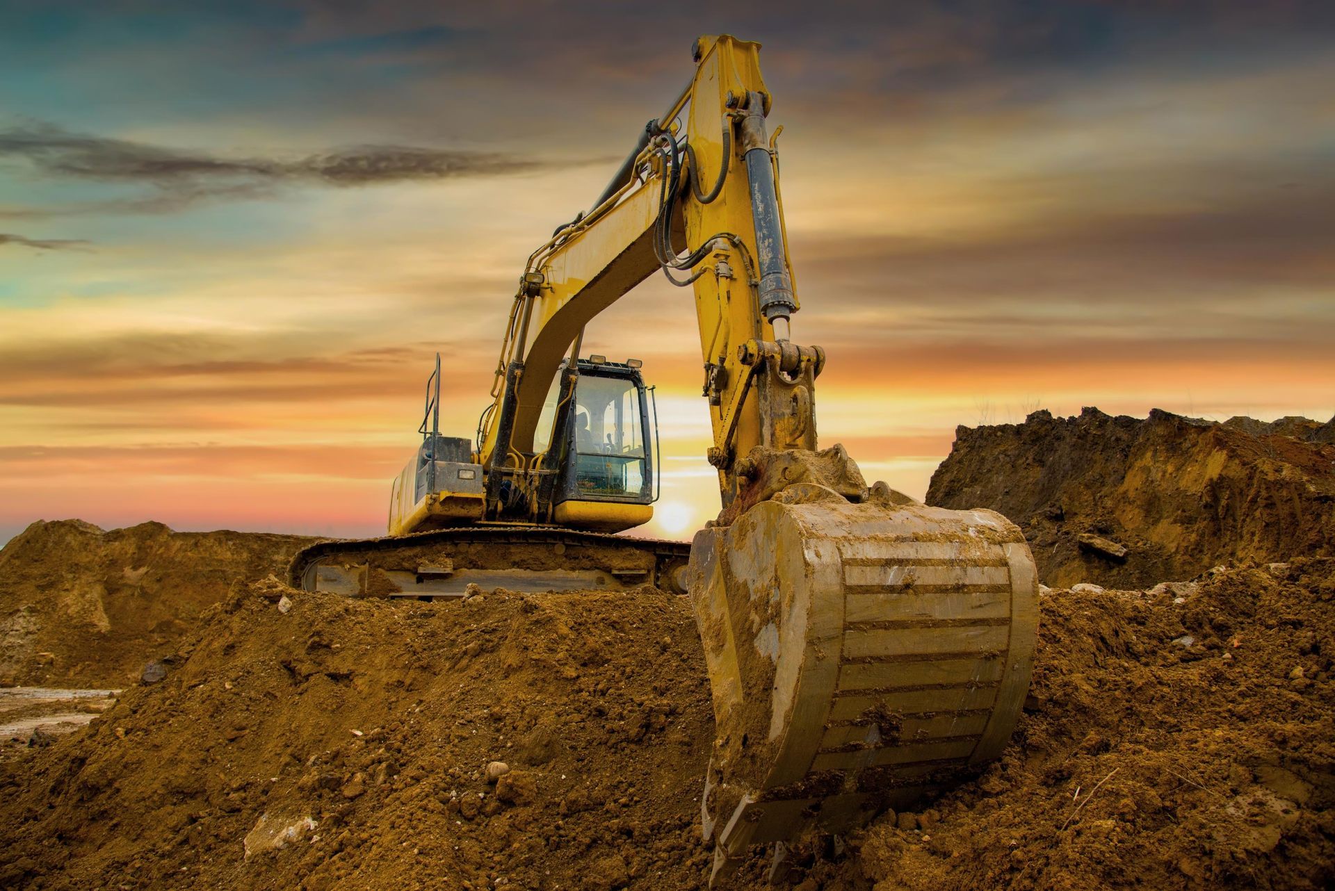 Yellow excavator digging a dirt mound at sunset on a construction site