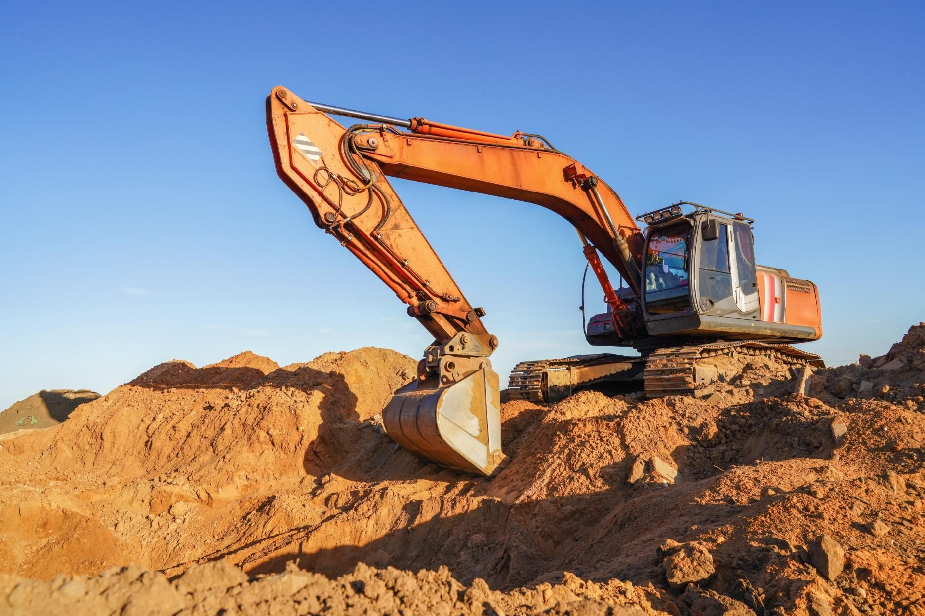 Orange excavator digging in a sandy dirt site under a clear blue sky