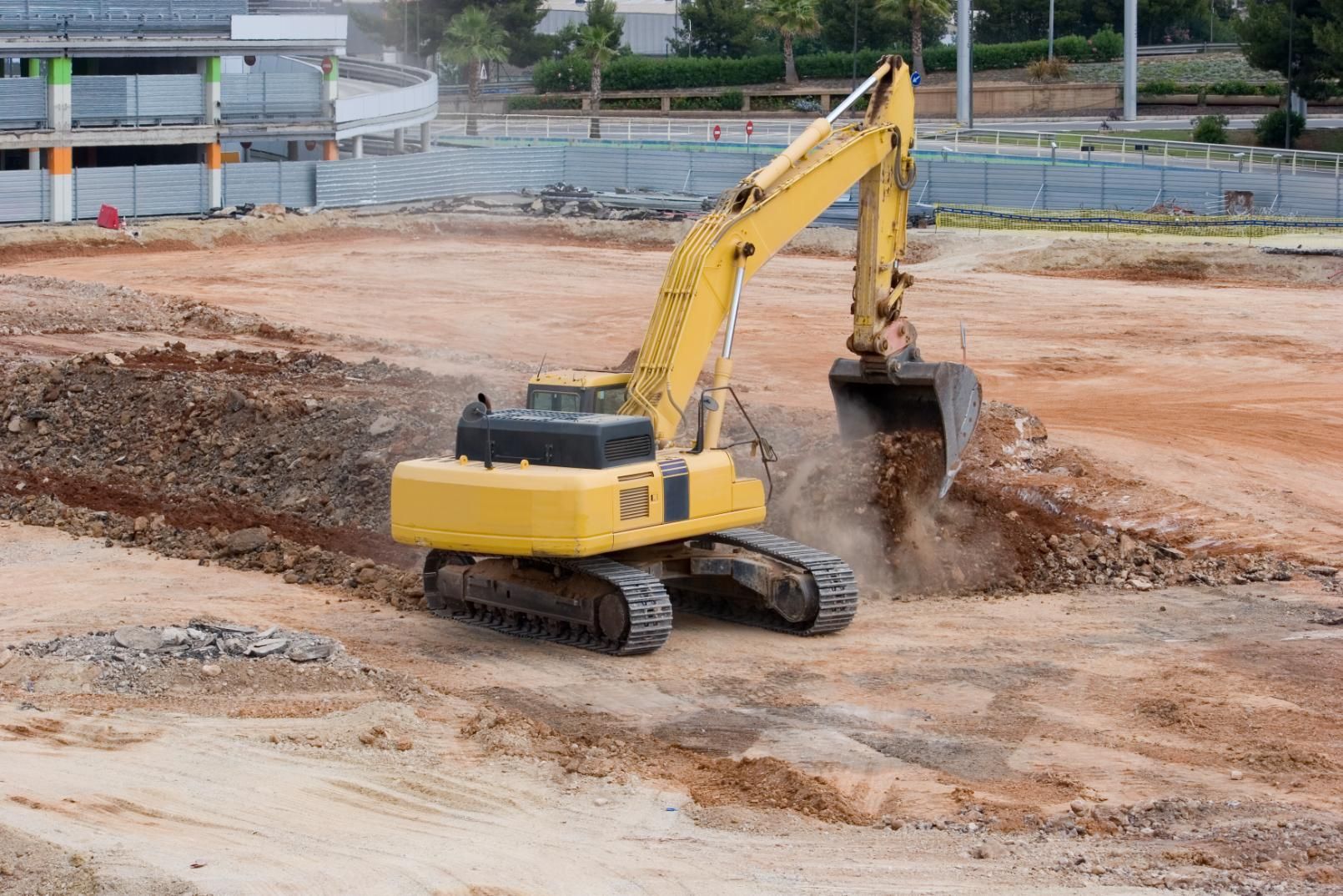 Yellow excavator digging dirt at a construction site, with mud and earth piles in the background