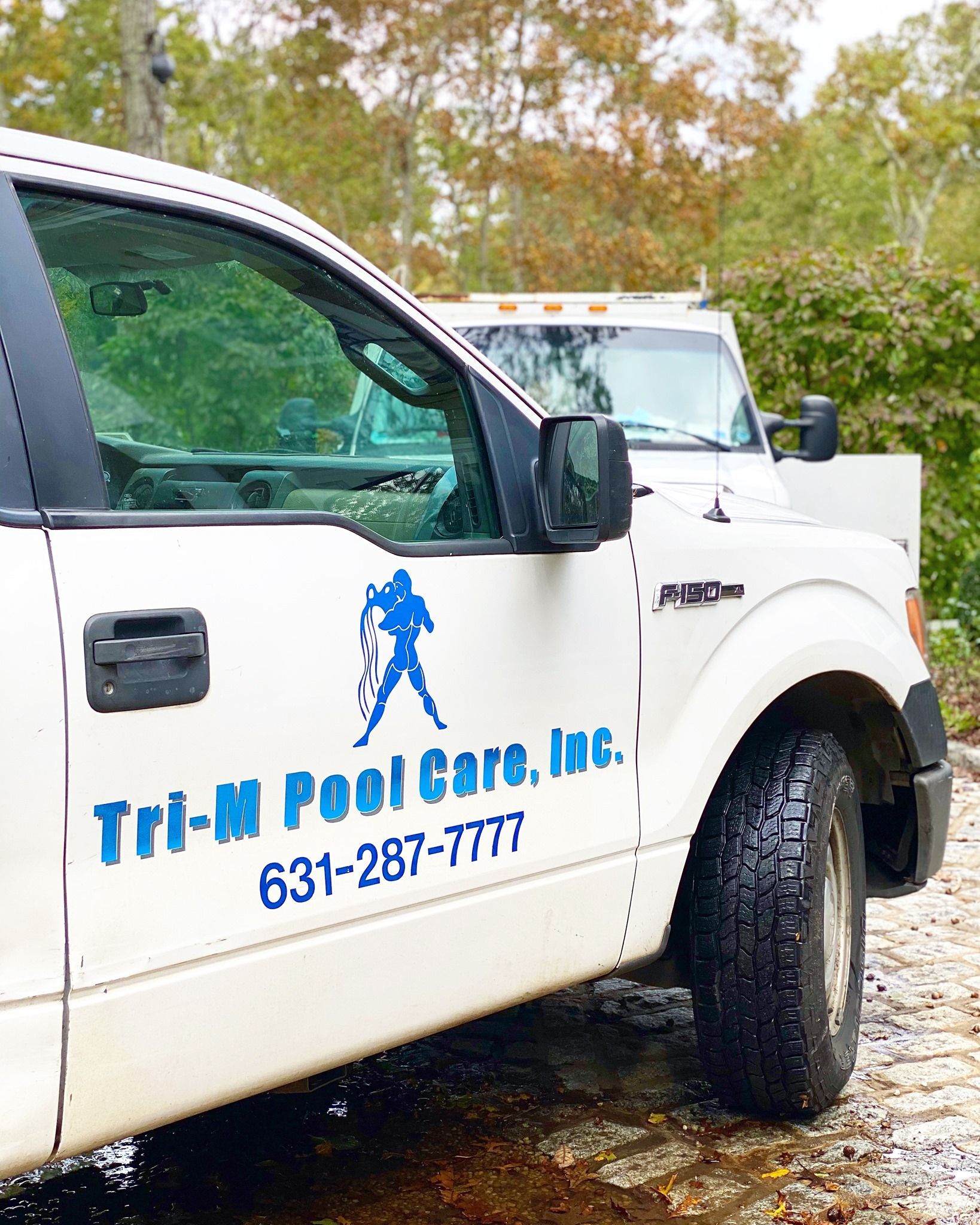 A side view of a white service truck parked outdoors, featuring the blue text 