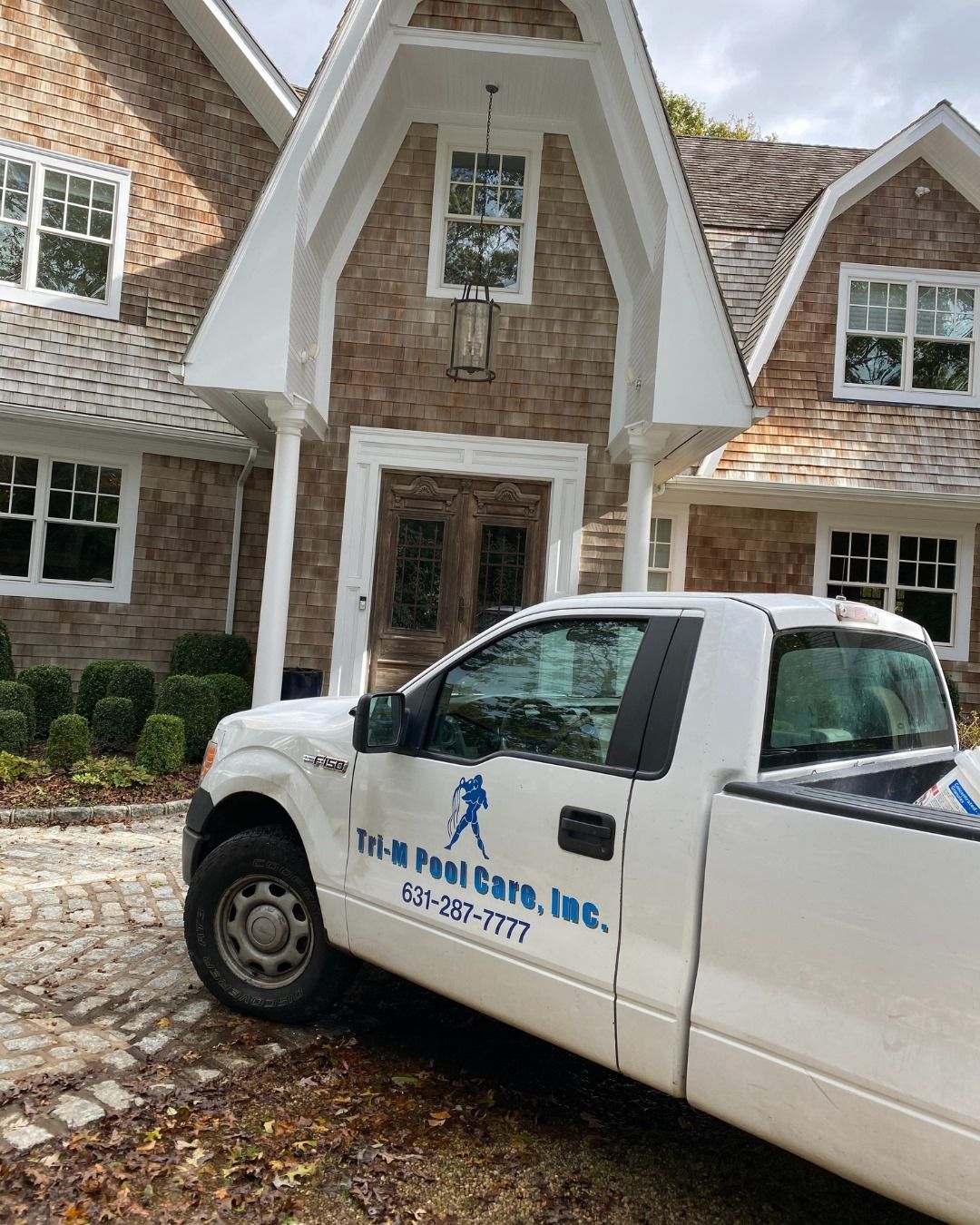 A white pickup truck parked in front of a tan brick house with a distinctive triangular entryway.