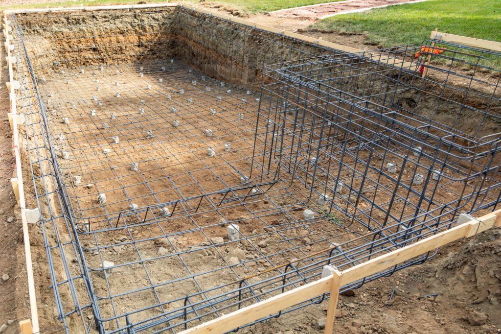 A swimming pool under construction, showing a dirt excavation reinforced with a grid of steel rebar.