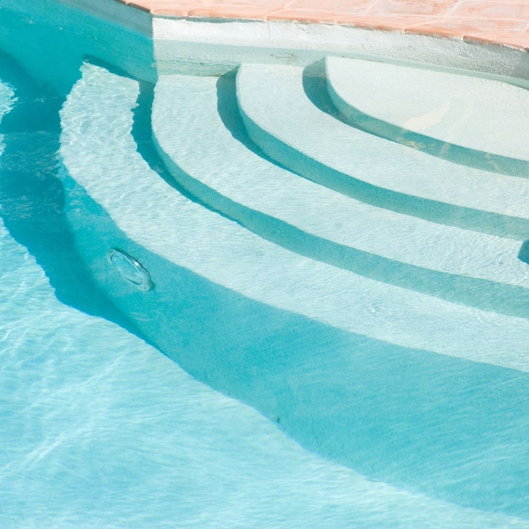 Sunlight illuminates turquoise water cascading down curved concrete steps into a bright swimming pool.