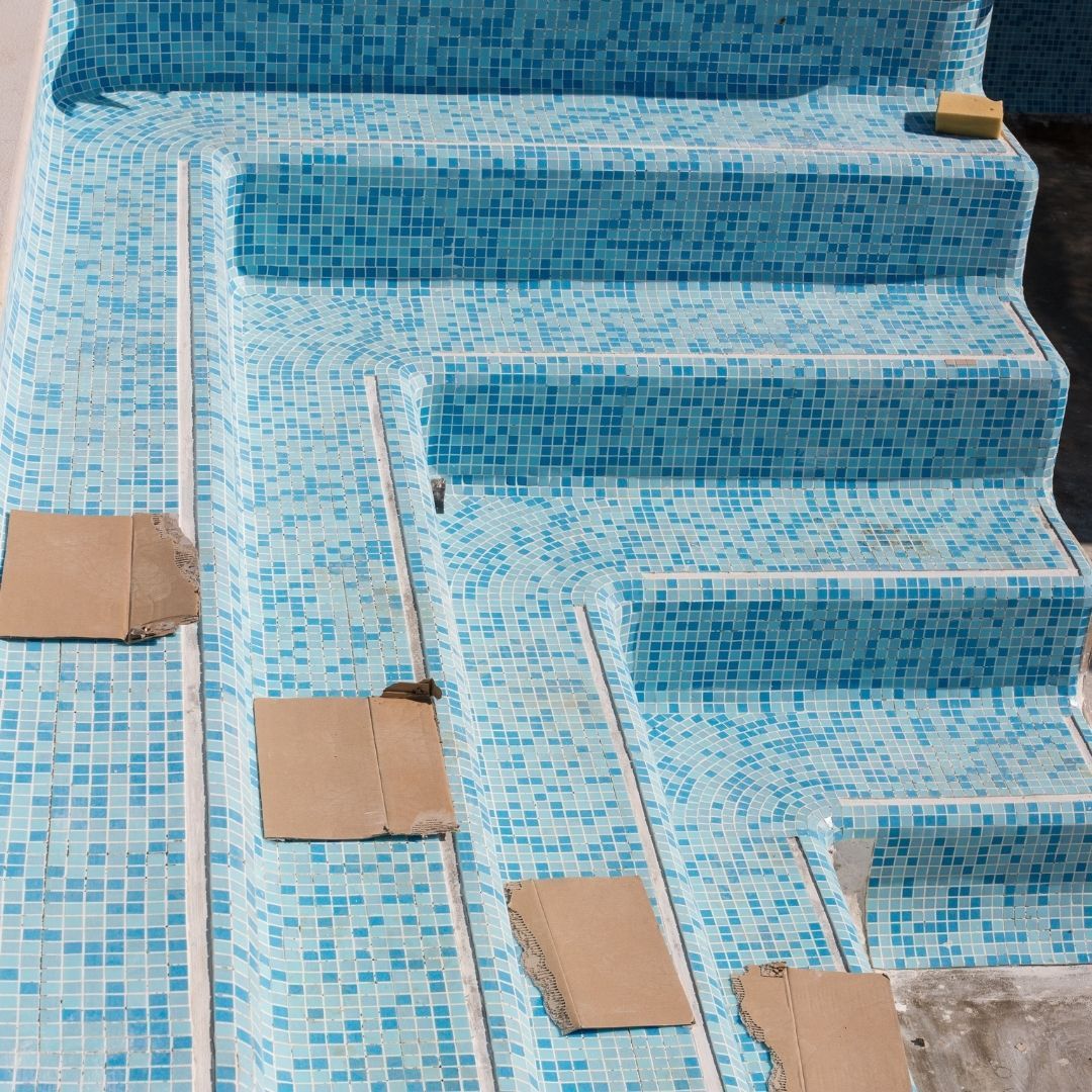 Blue mosaic tiled pool steps under construction with cardboard protectors placed on the horizontal surfaces.