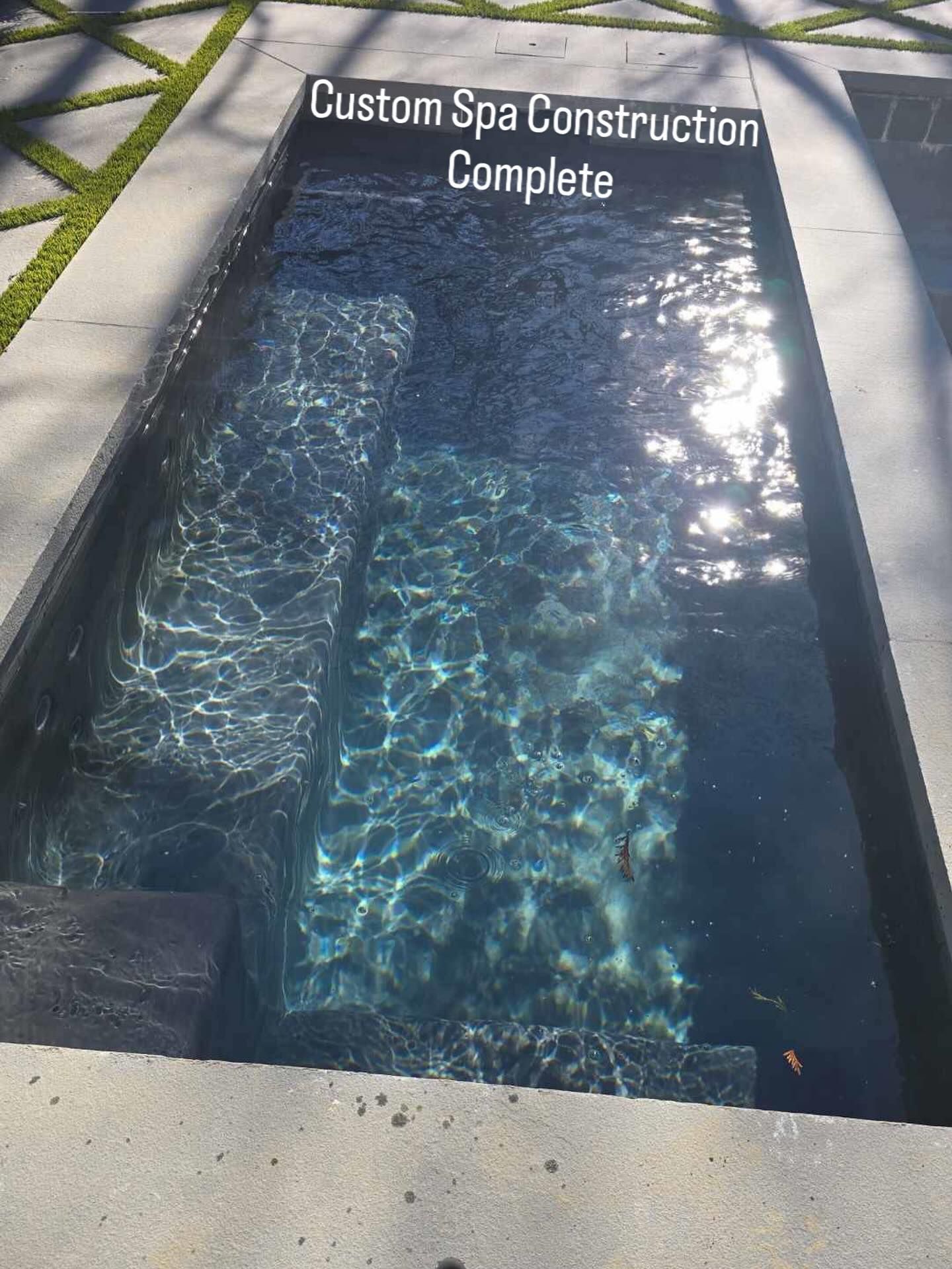 Stainless steel ladder leading into a swimming pool with dark blue square tiles.