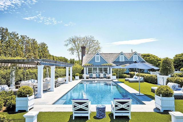 A gray stone patio and low retaining wall surround a swimming pool in a wooded backyard.