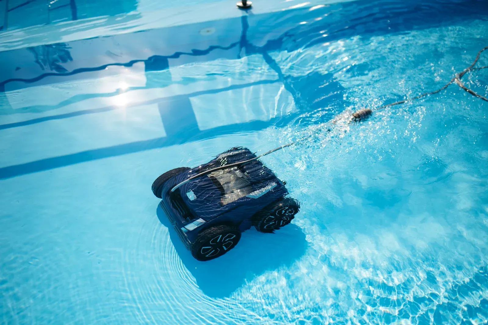 Small black robot underwater in a bright blue pool, leaving a trail of bubbles
