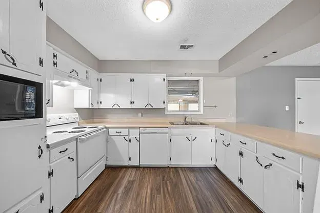 A kitchen with white cabinets and wooden floors