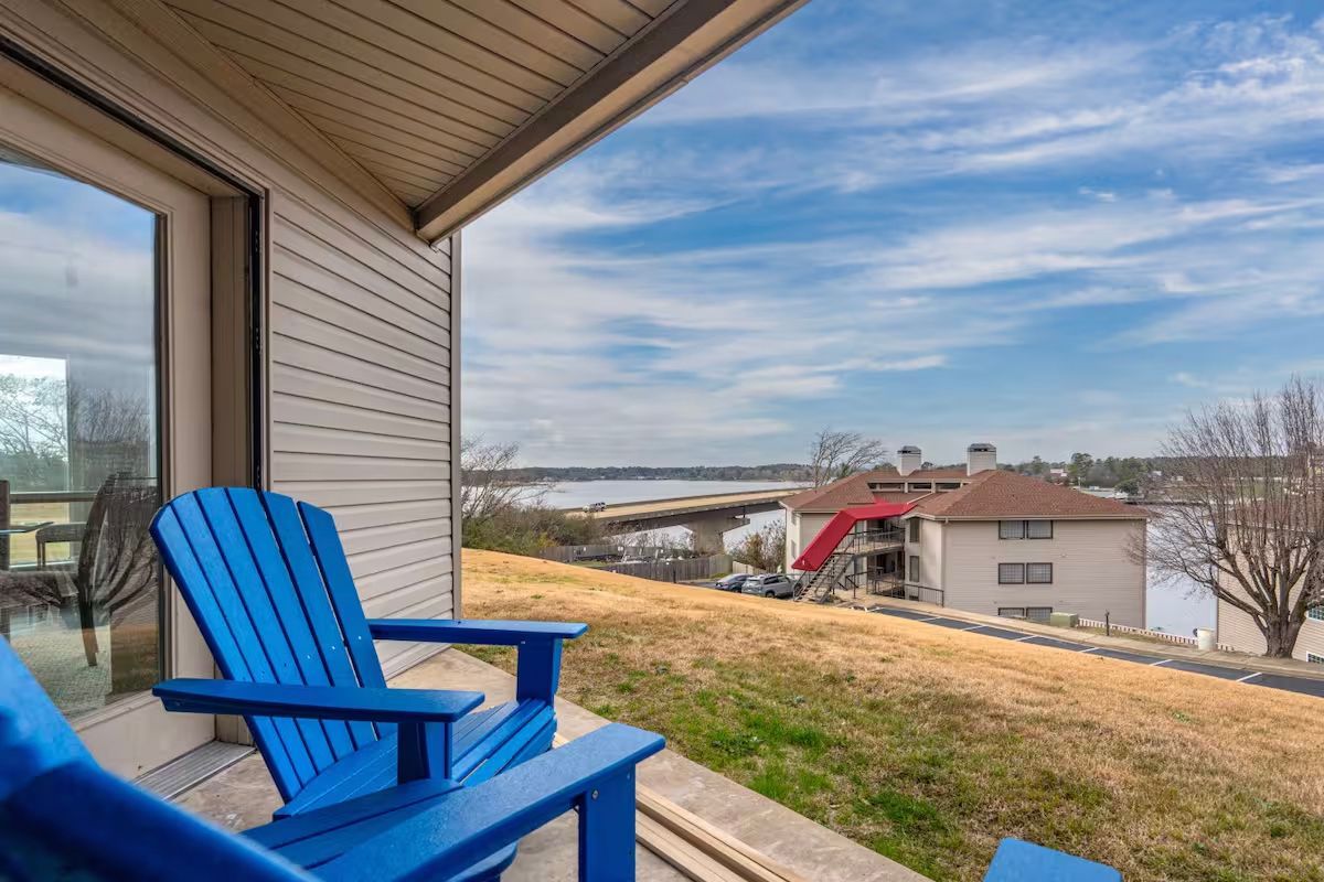 Two blue chairs are sitting on a balcony overlooking a lake.