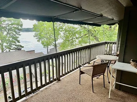 Balcony with a lake view. Brown wooden railing, two chairs, small table, and awning.