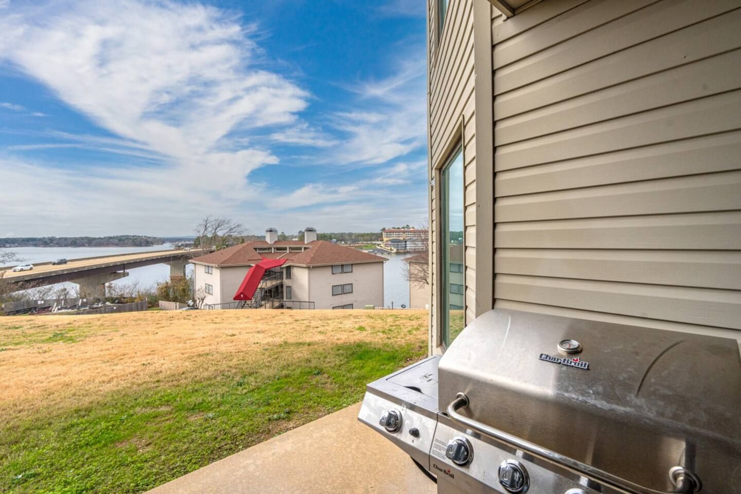 A grill is sitting outside of a house with a view of a lake.