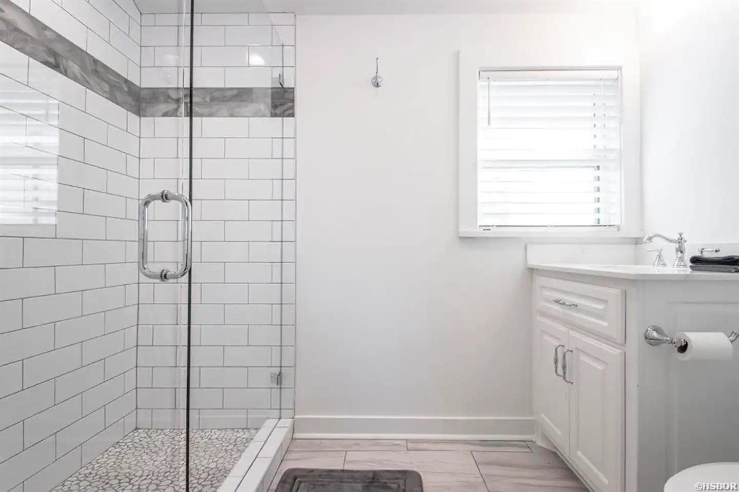A bathroom with a walk in shower , sink , toilet and window.