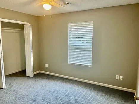 An empty bedroom with a window and a ceiling fan.