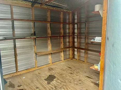 A shed with wooden shelves and a metal wall.