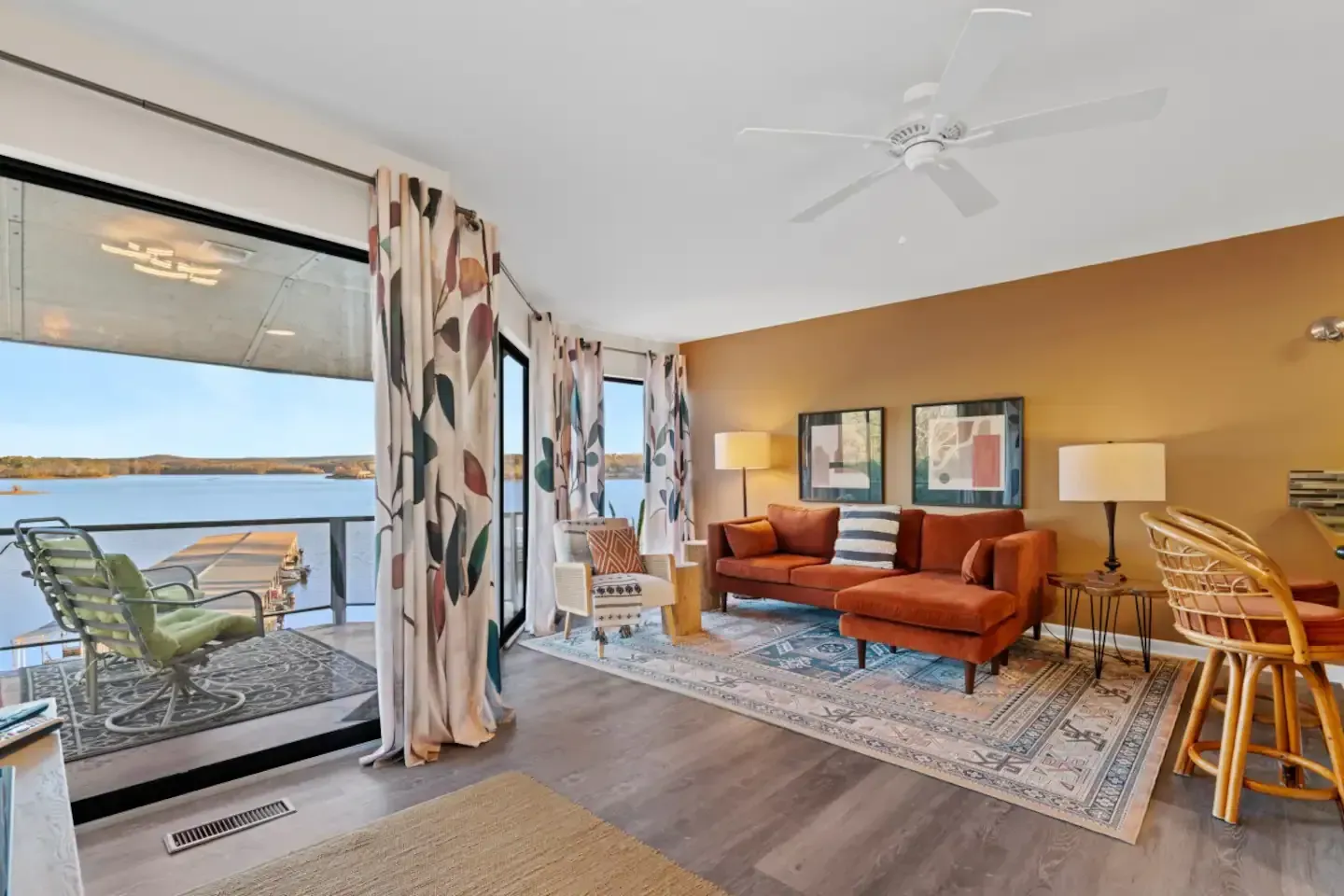 A living room with a couch , chairs and a ceiling fan overlooking a lake.